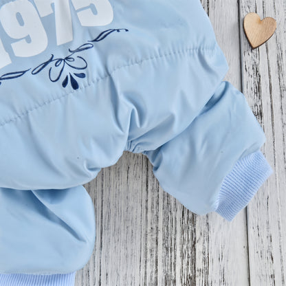 Close-up of a light blue dog jumpsuit leg and cuff, with '1975' print detail, displayed on a white wooden background with a wooden heart ornament.