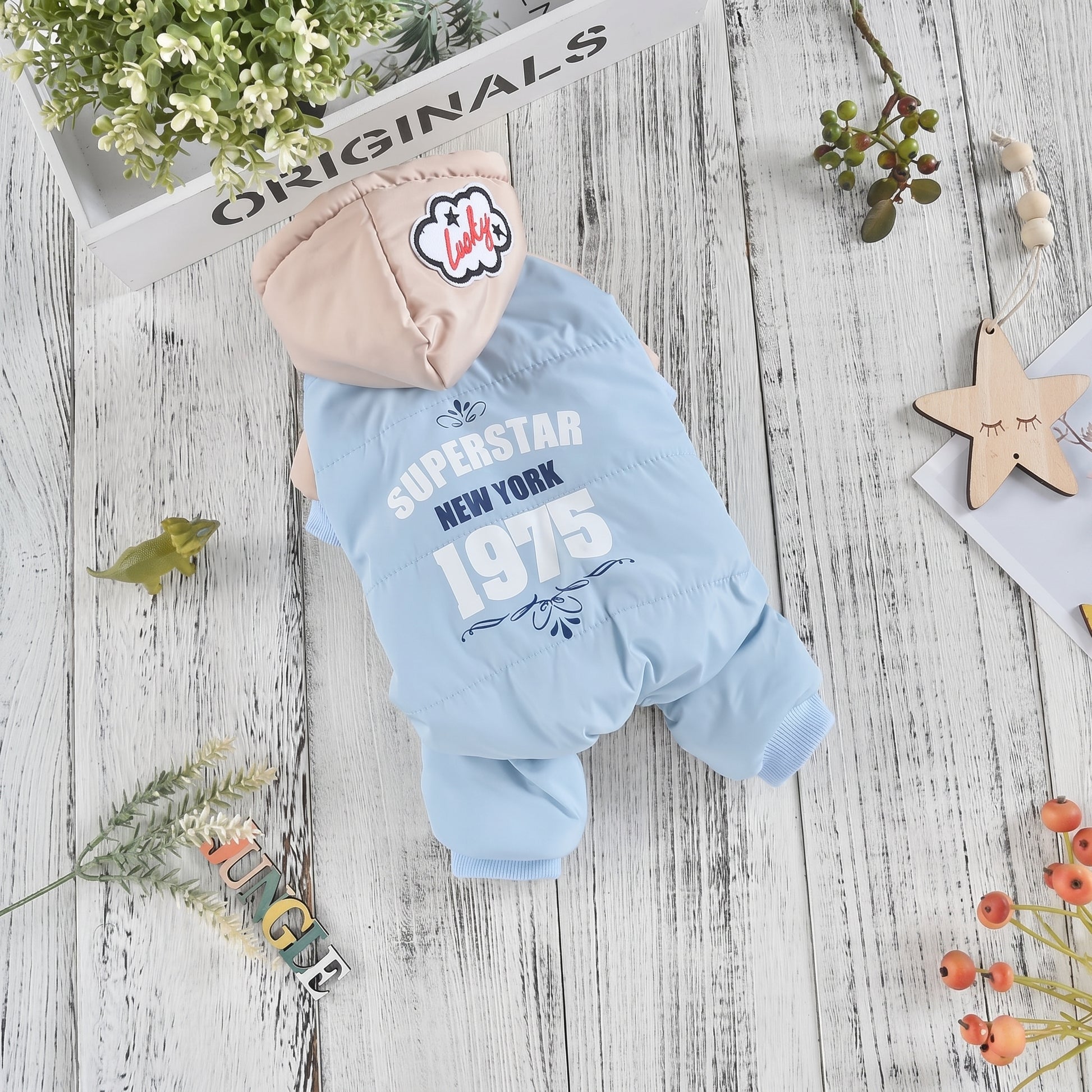 CozyCloud Full-Body blue dog jumpsuit with a hood, featuring 'Superstar New York 1975' print, displayed on a rustic wooden table.