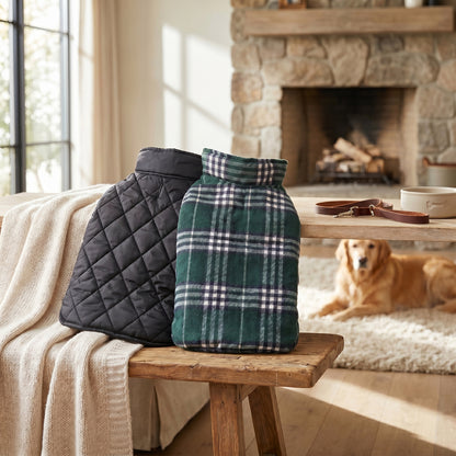 Black quilted vest and green plaid reversible dog coat displayed on a wooden bench, with a golden-colored dog resting in the background.