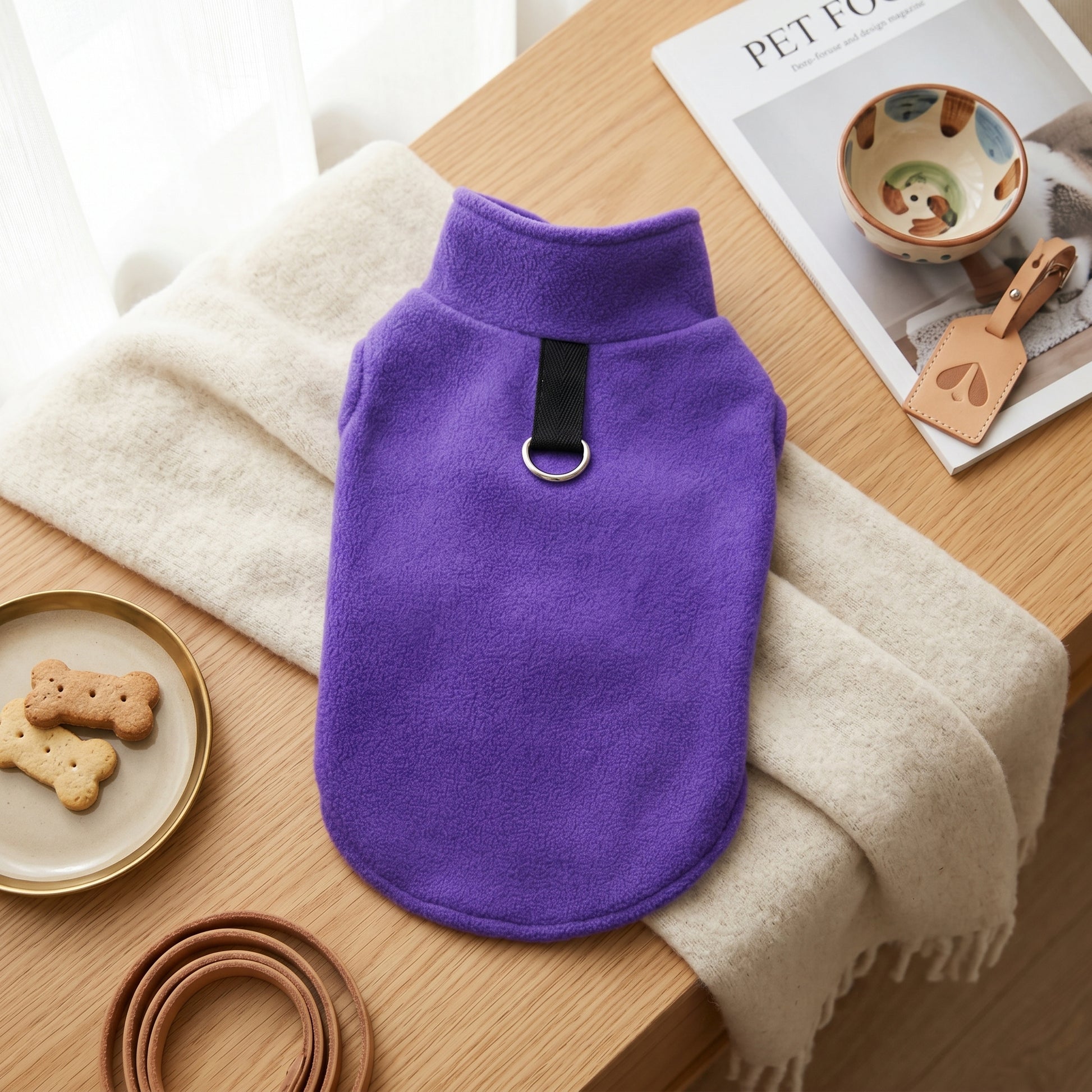 Purple fleece dog sweater displayed on a wooden surface next to a bowl of treats and a leather leash.