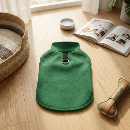 Green fleece dog sweater displayed on a wooden floor next to a dog bed, a book, and a dog treat toy.