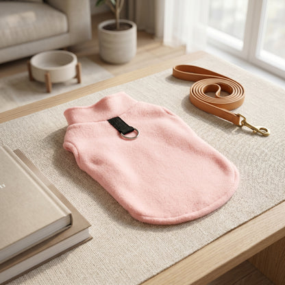 Simple pink fleece dog sweater with a leash attachment D-ring, displayed on a textured beige surface with a matching leash.