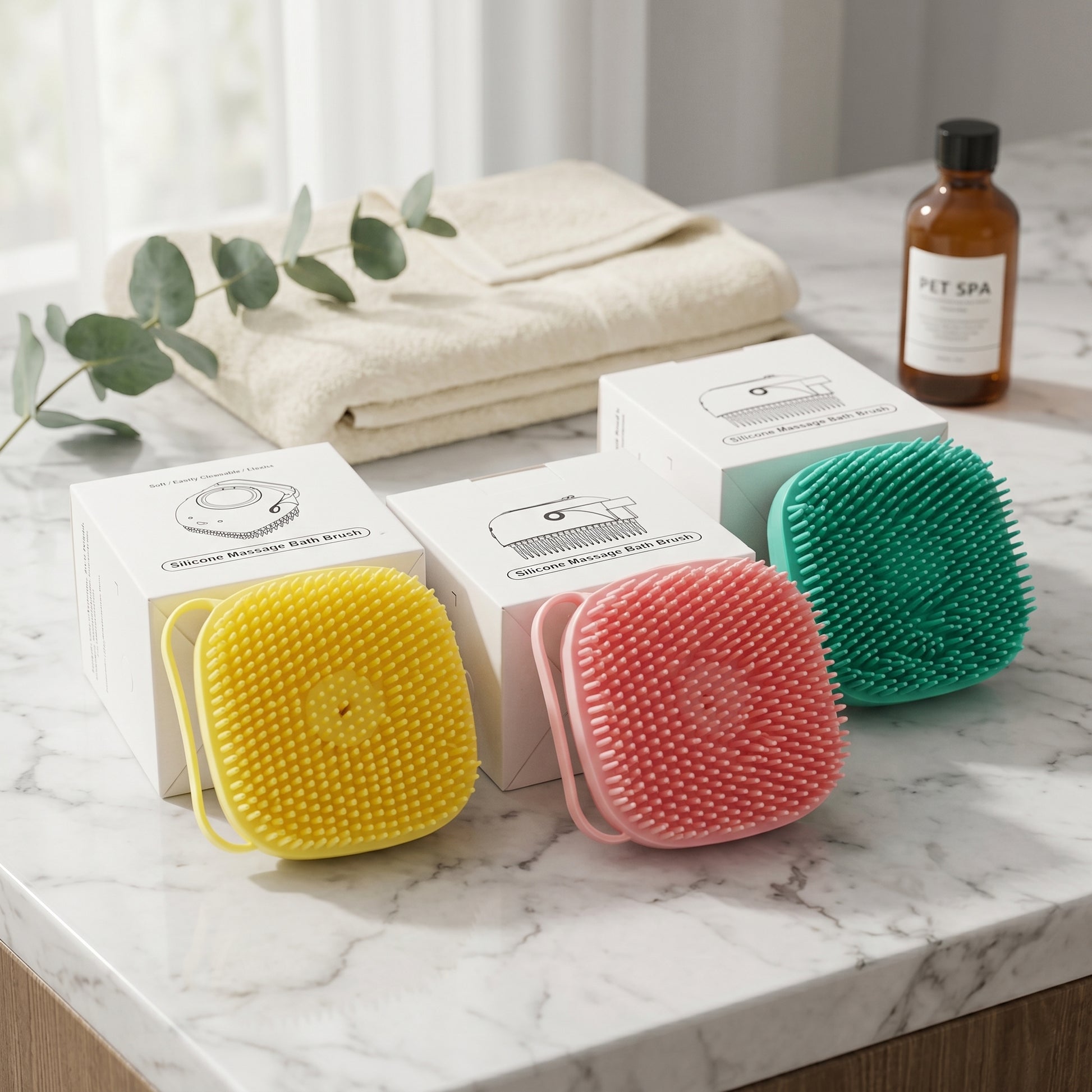 Three BathFlow silicone grooming brushes in yellow, pink, and teal, resting on a marble counter alongside their product packaging and a bottle of shampoo.